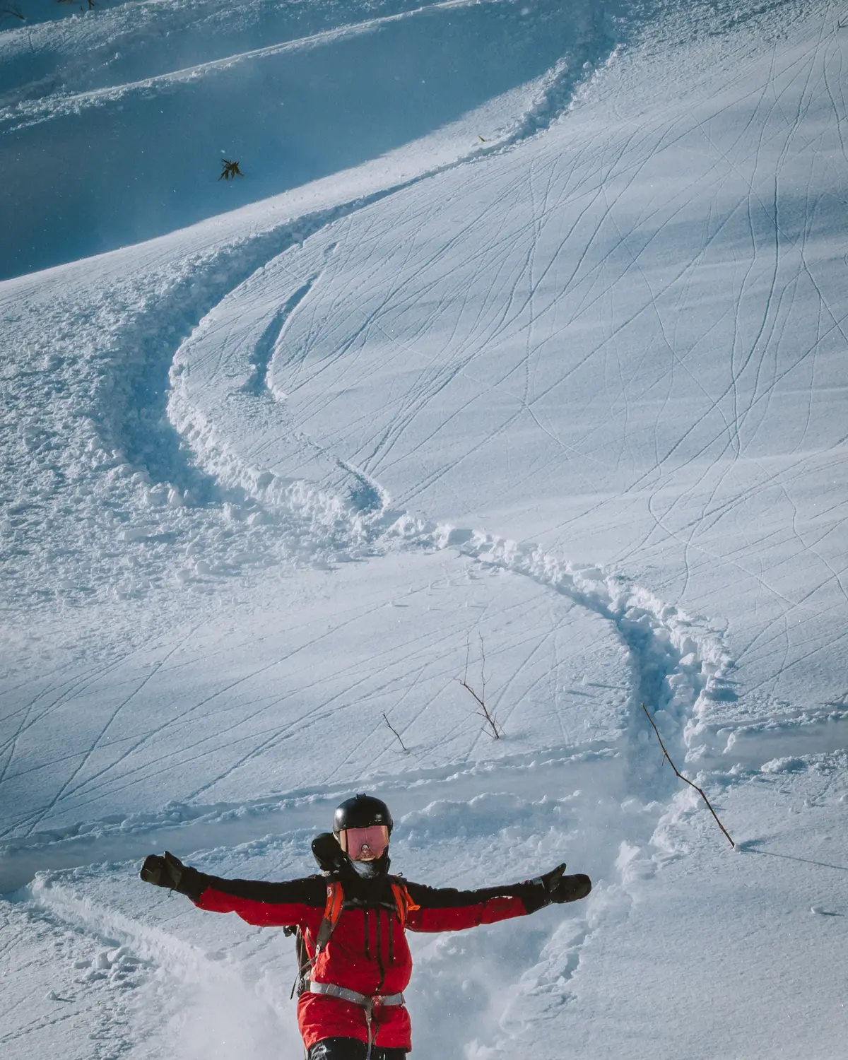 Rider in giacca rossa a braccia aperte nella powder, con la sua traccia che scende dal pendio